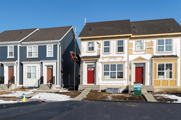 Two multi-family homes under construction, one with blue siding and one with yellow siding, in Edmonton.